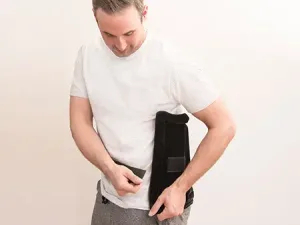 A man applying a heating pad to his back