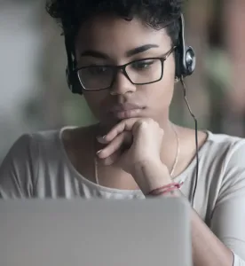 A woman looking at a laptop and wearing headphones