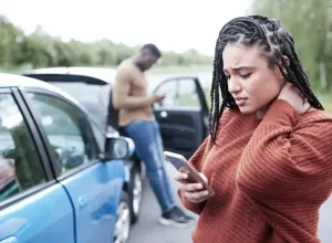 A woman using a cell phone while holding her neck after a car accident