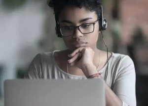 A woman looking at a laptop and wearing headphones